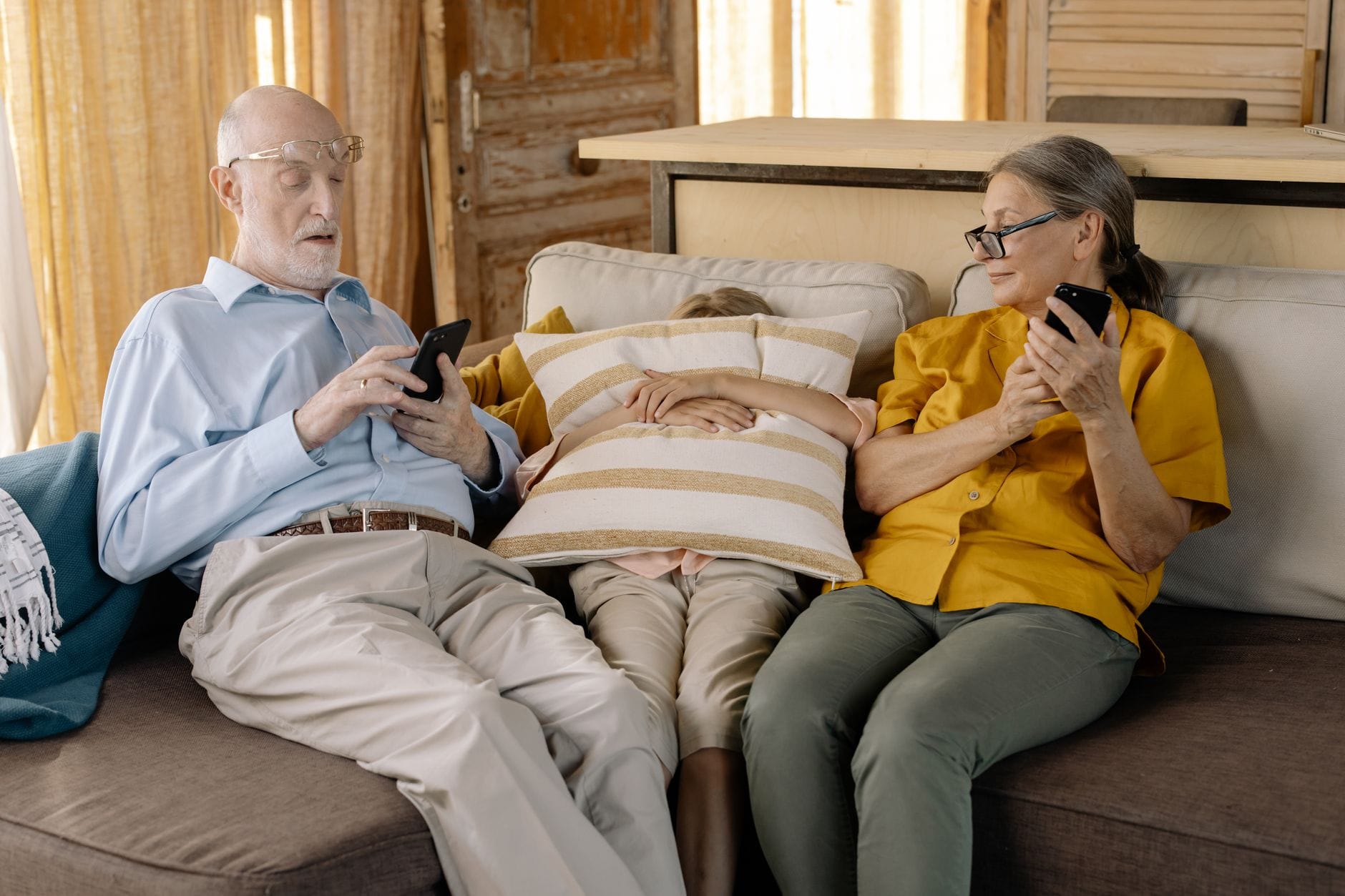 Seniorzy na kanapie z wnukiem, wspólnie korzystający ze smartfonów