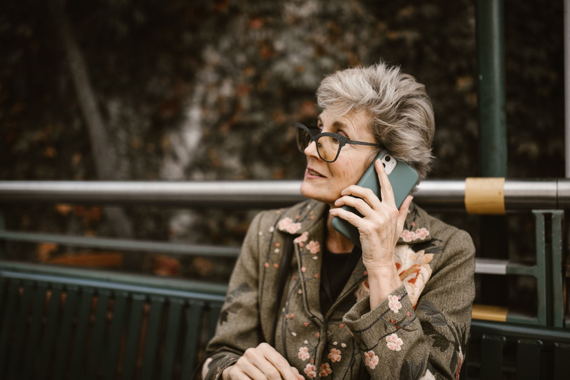 Nowoczesne aplikacje dla seniorów: zdrowie, pamięć, zakupy i kontakt z rodziną Starsza kobieta w okularach rozmawia przez smartfon na świeżym powietrzu