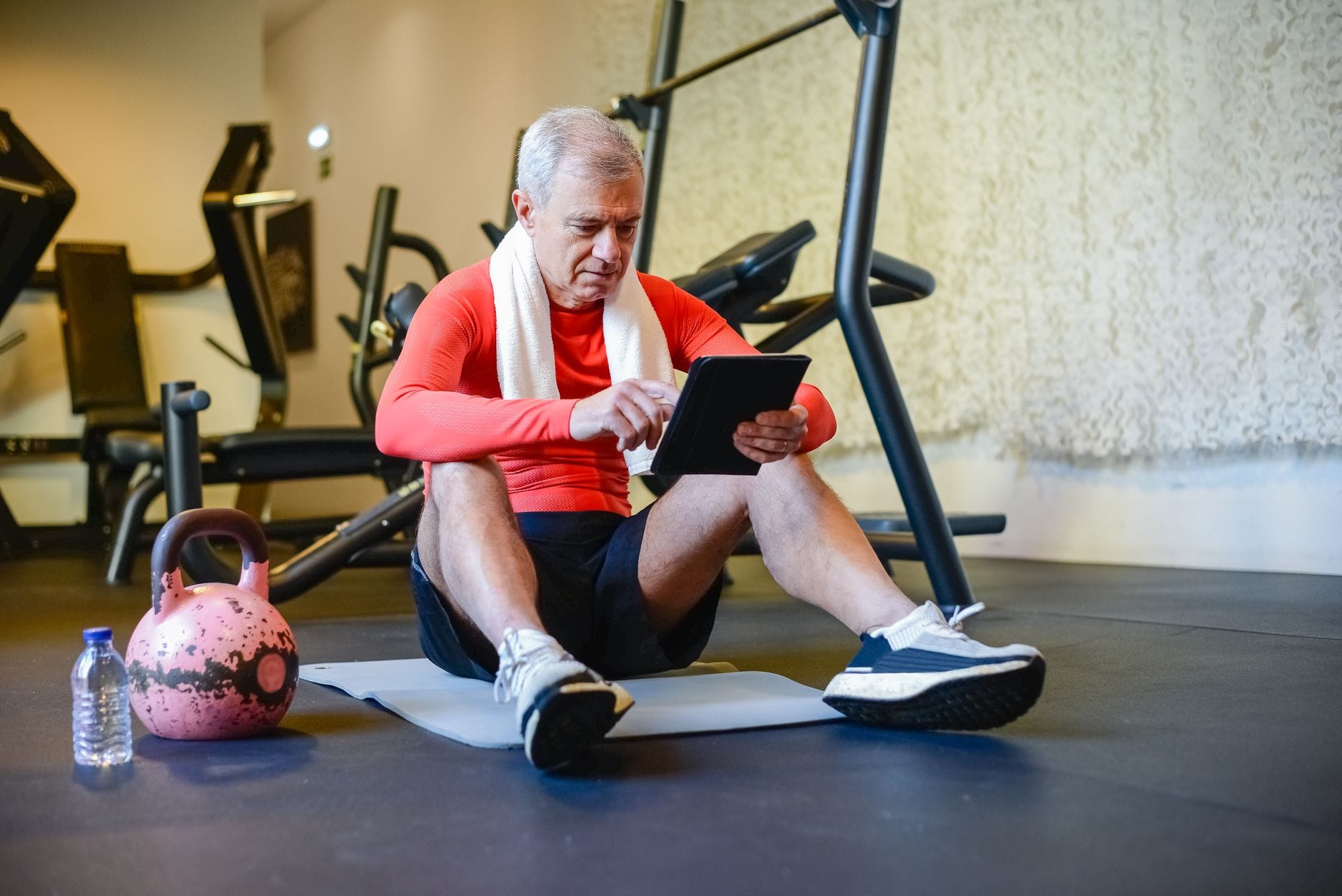 Starszy mężczyzna na macie w domowej siłowni korzysta z tabletu Starszy mężczyzna na macie w domowej siłowni korzysta z tabletu