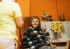 Odzież adaptacyjna dla osób leżących i z ograniczoną sprawnością – gdzie kupić i co wybrać? Seniorka w fotelu w domu opieki z opiekunką obok