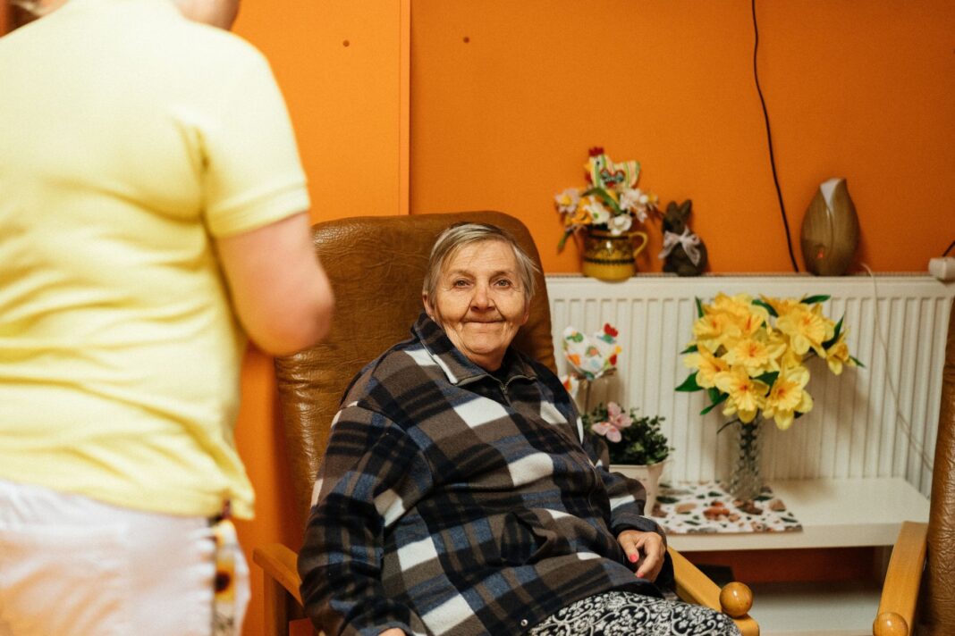 Seniorka w fotelu w domu opieki z opiekunką obok Seniorka w fotelu w domu opieki z opiekunką obok